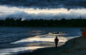 Runner's silhouette on the stormy beach, stormy clouds on the sky, light reflecting on the sea